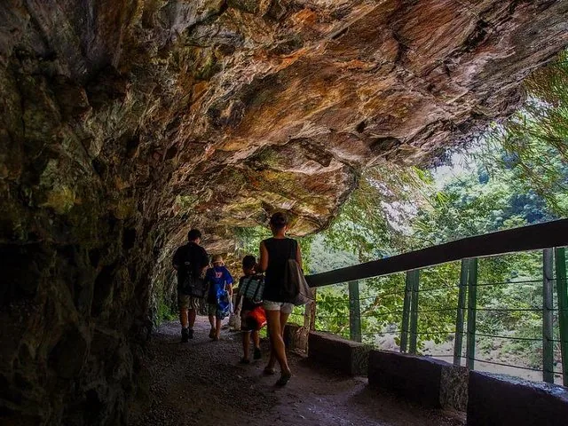 A group of people walking along a dark tunnel path carved into rock.