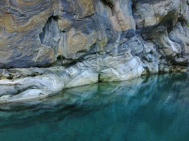 Close-up of layered marble rock formations reflected in clear, turquoise water.