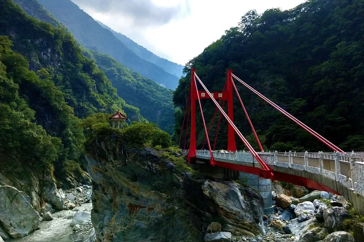 A bright red bridge spanning a river canyon next to a small cliffside pavilion.