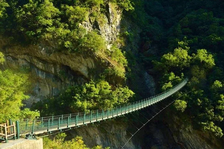 A long suspension bridge spanning across a deep, lush green gorge.