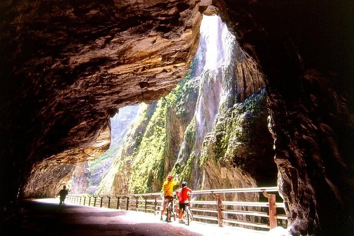 A group of people wearing helmets walking along a narrow gorge pathway.