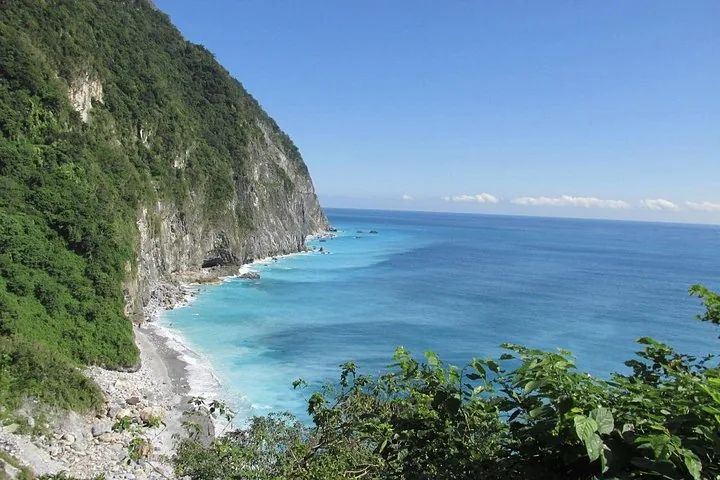 Steep, lush green cliffs dropping into the bright blue ocean in Taiwan.