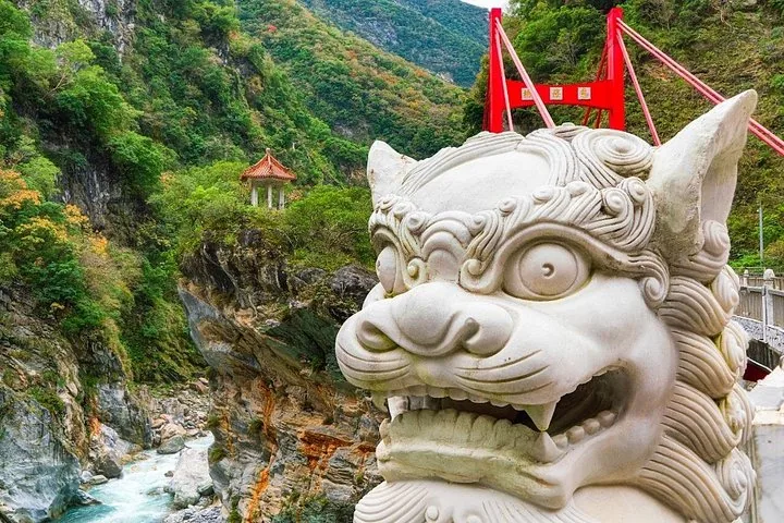 Close-up of a white marble lion statue with a red bridge and pavilion behind.