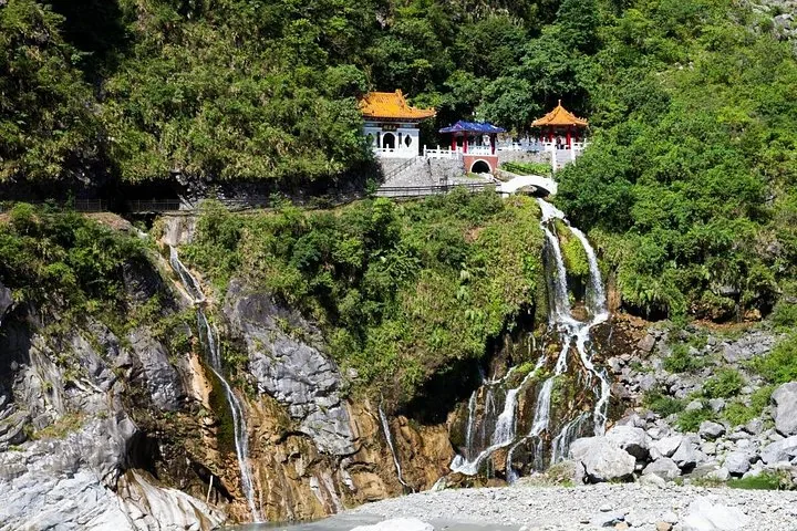 A waterfall cascading down rocky cliffs below traditional pavilions at Eternal Spring Shrine.